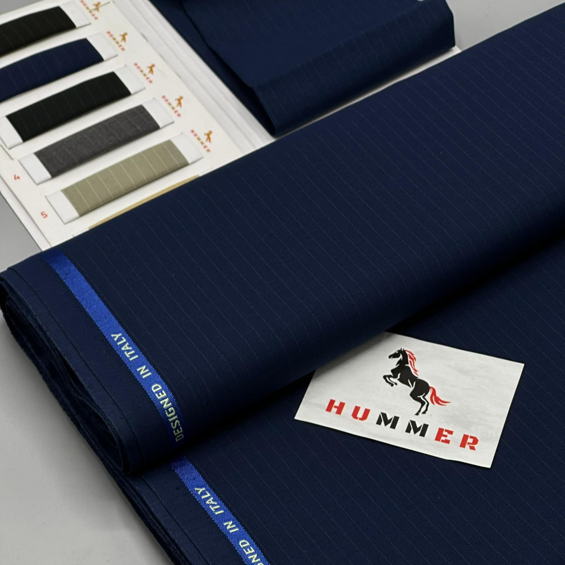 Bolts of navy suiting fabric fanned out beside grey and black swatches