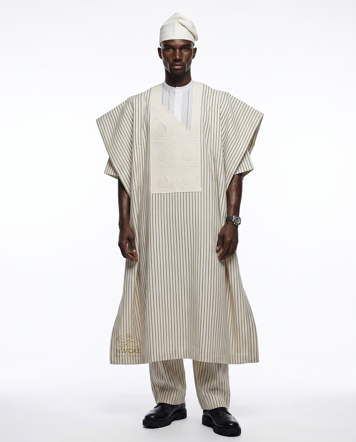A model in the Ivory Stripe Agbada with an embroidered chest panel and white fila